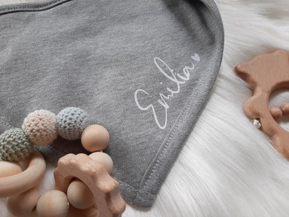 Nahaufnahme vom Dreiecktuch für Baby.  Schriftzug ist gut erkennbar. Das Dreiecktuch ist aus Baumwolle und wird durch Druckknöpfe verschlossen.Personalisiere dein eigenes Dreiecktuch mit deinem Wunschnamen. Angenehmer Tragekomfort, weich und wärmend