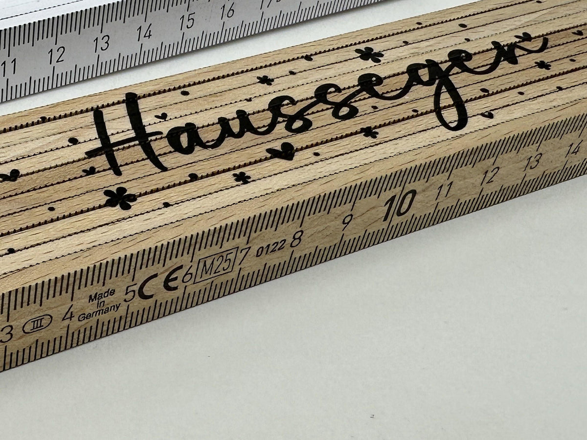 Nahaufnahme Meterstab Natur aus Holz mit Haussegen in Schreibschrift, Herzen und Blümchen (Motiv 4) und Zentimeter-Skala